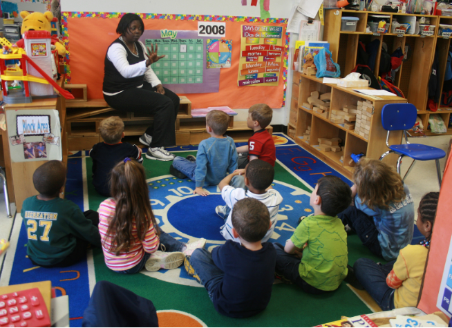 A group of kindergarteners sit on the carpet listening to their teacher tell them about the months of the year. Teenagers feel nostalgia when remembering how they used to sit on the carpet in elementary school.
(Courtesy woodleywonderworks via Wikimedia Commons)