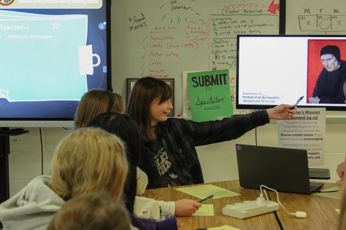 Senior Marcy Harper, co-editor-in-chief of Spectator, gestures to a piece of art being reviewed by the Spectator staff. "I’m very uninvolved in the discussion about what gets in and what doesn’t get in, aside from if any of the executive heads need me to step in,” English teacher and Spectator's adviser Alexia Remy said.