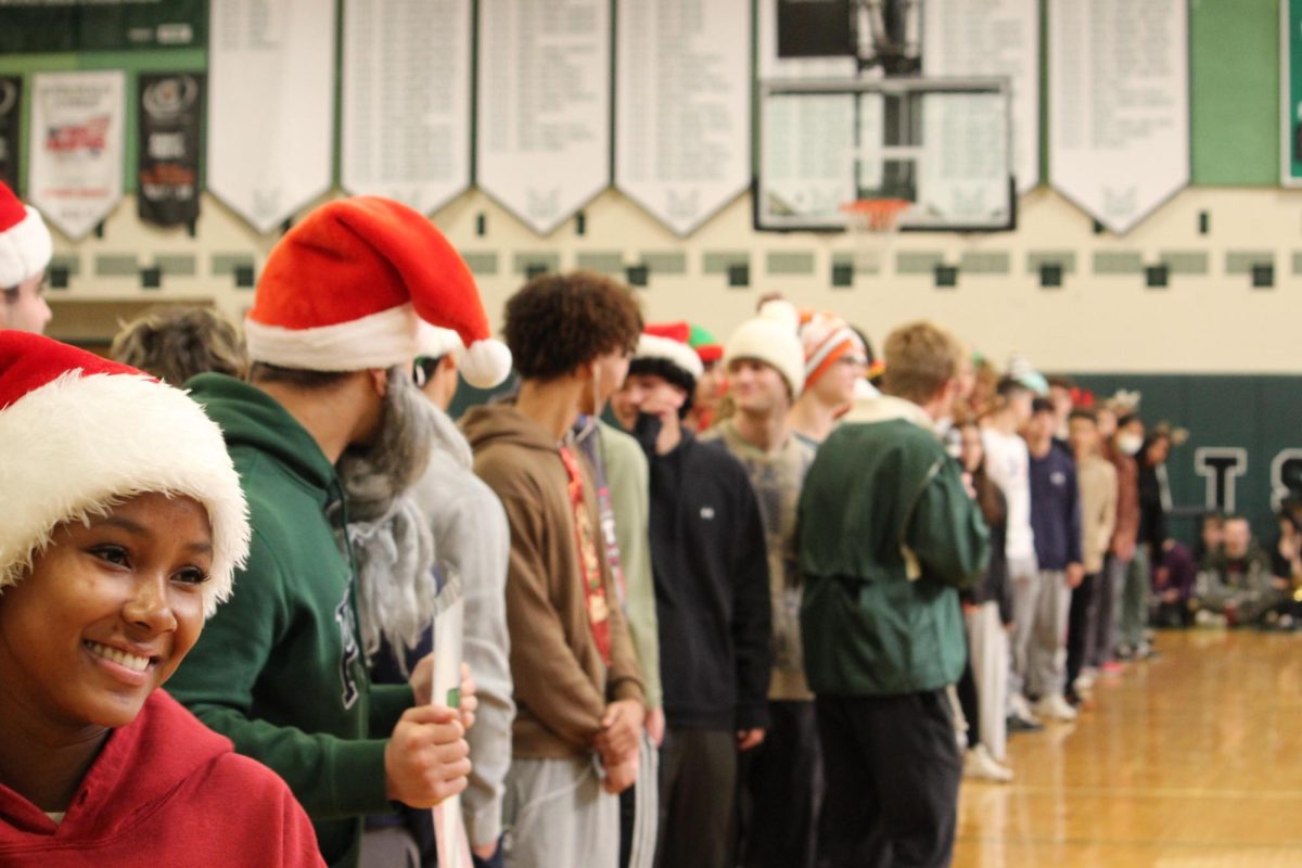 The track team lines up in front of the crowd in Christmas-themed costumes. Track is the largest sports team at WJ with over 80 members, and the line spanned almost the entire width of the gym.