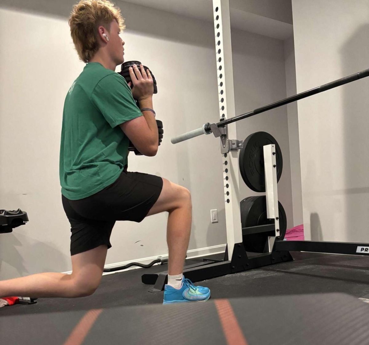 Senior Connor Mcgee performs a split squat in his home gym. Weightlifting is crucial for athletes to maintain and build up their strength in the off-season.