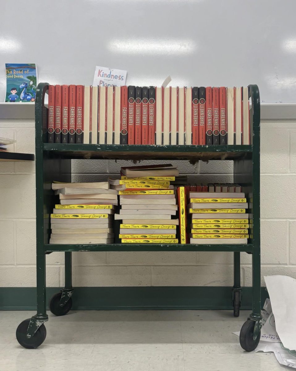 Dozens of books sit on a rolling cart, ready for students to take.  The new and redesigned 10th-grade English curriculum has brought controversy and widely felt change, one that has not been smooth.