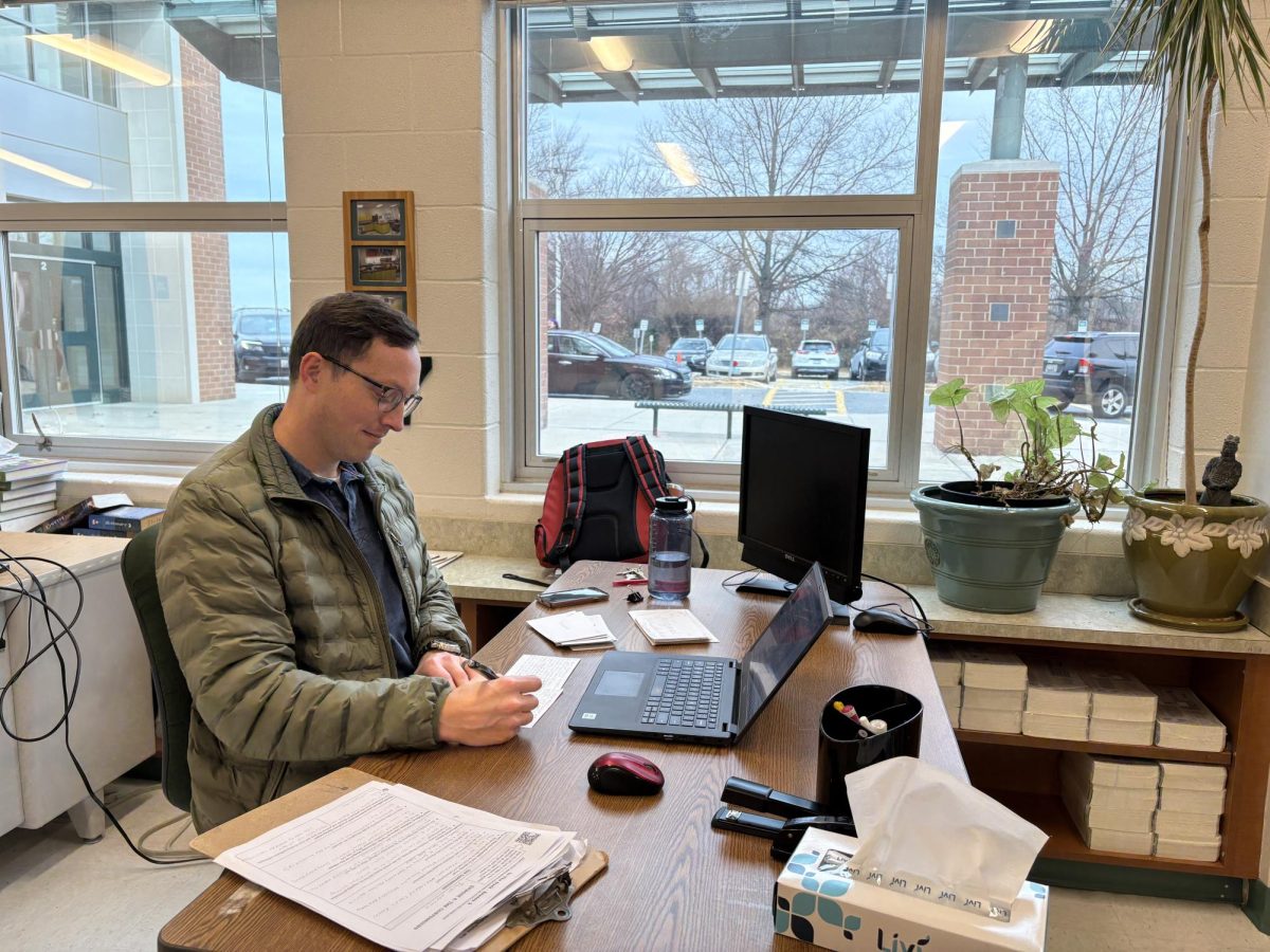 History teacher Tobias Meier works in the Social Studies office during his off period while his classroom is being used by another teacher. Meier has a "go with the flow" personality and is willing to move out of his classroom to allow the room to be used by another teacher.