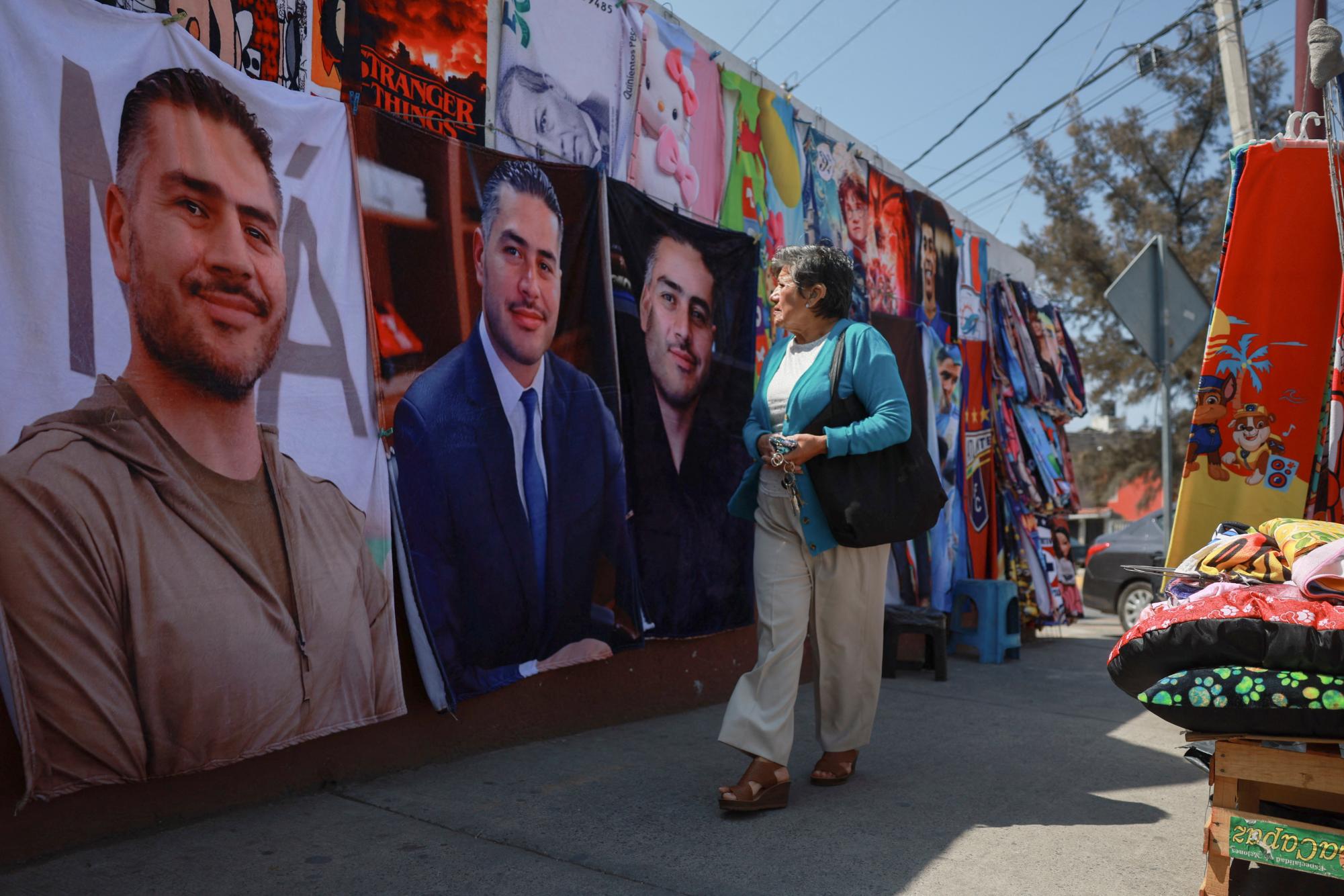 A woman looks at merchandise at street stalls selling blankets featuring Mexico's 44-year-old Security Minister Omar Garcia Harfuch, whose popularity has surged after cartel leader El Mencho's death, along a sidewalk in Ecatepec, State of Mexico, Mexico, March 12, 2026. (REUTERS/Henry Romero)